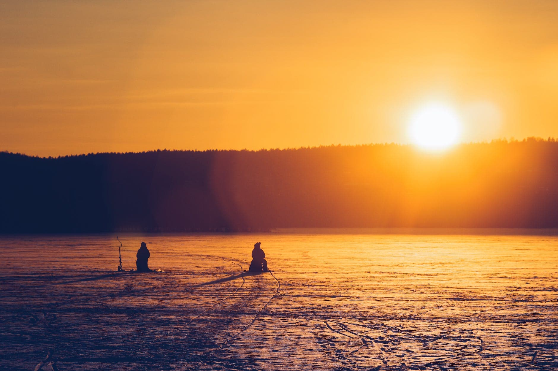 silhouette of two persons sitting while ice fishing on an iced covered body of water at dawn